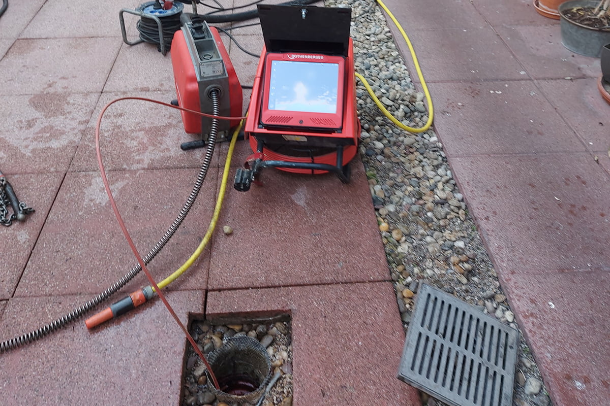 Ausrüstung zur Kanalinspektion mit Kamera und Schläuchen neben geöffnetem Bodenabfluss